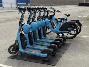 Rental e-scooters and bicycles parked in a line.