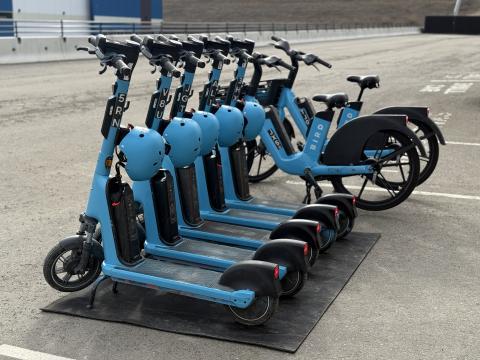 Rental e-scooters and bicycles parked in a line.