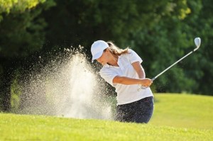 A woman swings a golf club in a sand trap.