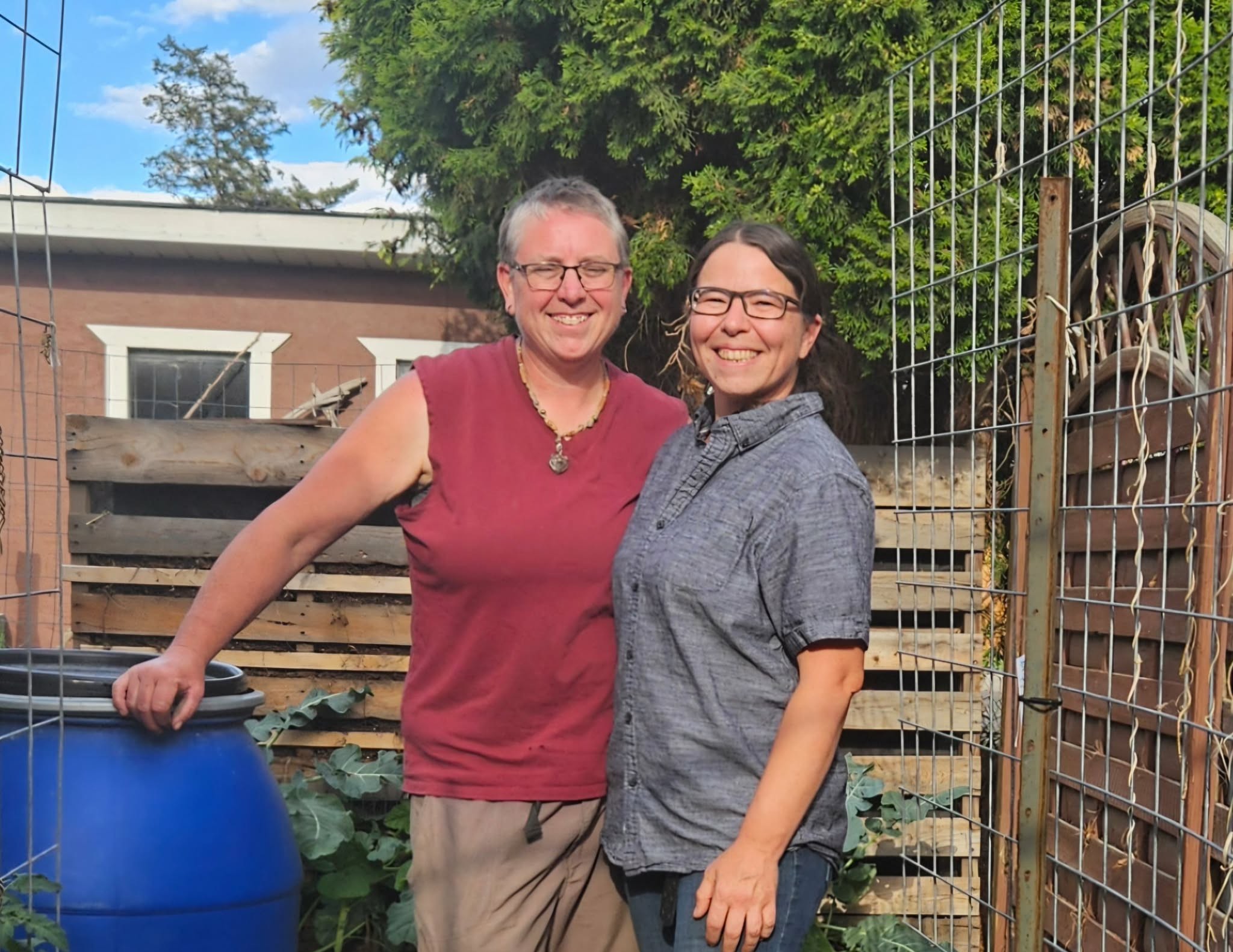 Two women stand together smiling in a garden.