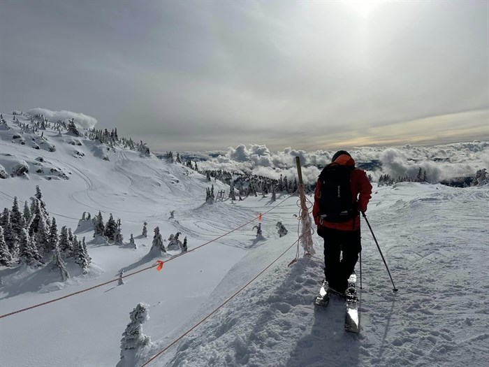 A person on skis looking out at the clouds while on a snowy mountain at Big White Ski Resort.