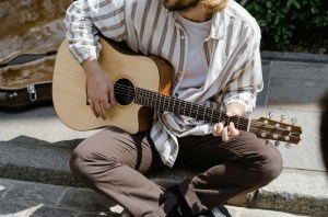 A picture of a guy holding a guitar sitting on a curb.