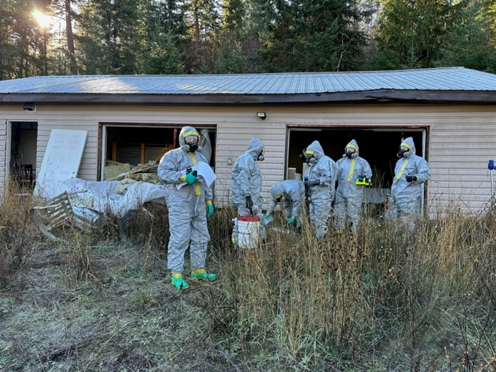 Police in hazmat suits search a shed.