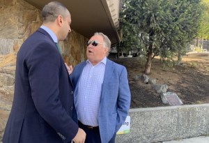Two men in suits have a conversation on a sidewalk.