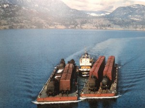 An old photograph shows a tugboat pushing two barges with rail cars on them on Okanagan Lake.