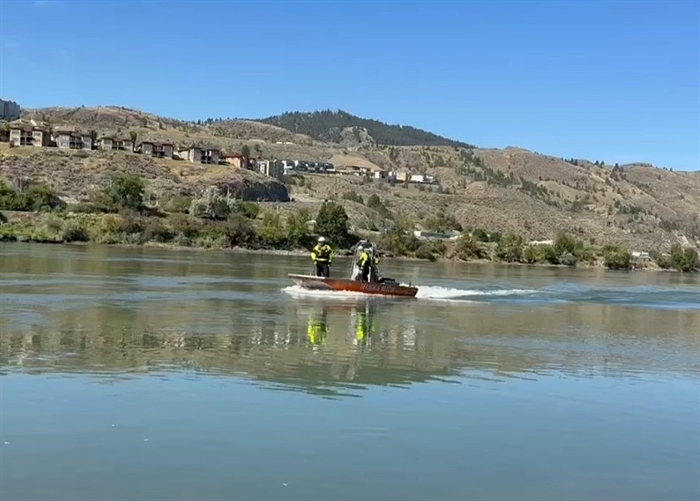 An aluminum boat carries two people on a river.