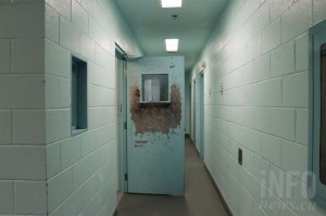 A hallway of holding cells with an open metal door
