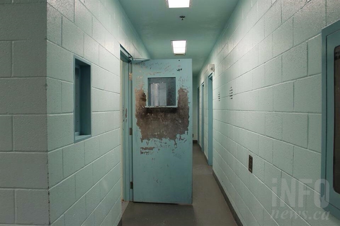 A hallway of holding cells with an open metal door