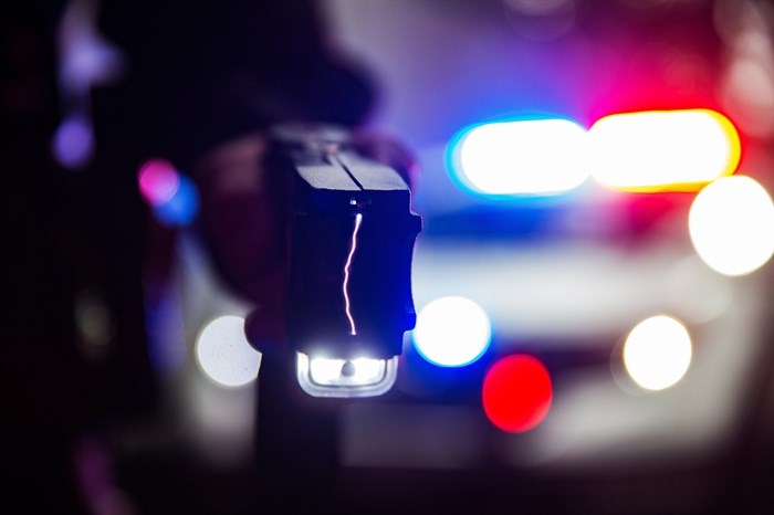 An activated conductive energy weapon with police lights in the background.