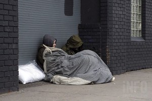 A phot of two homeless people huddled together under blanket.
