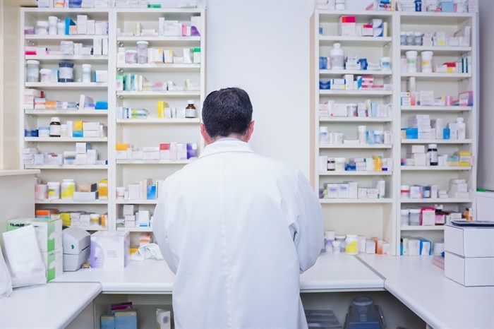 A pharmacist works at a counter facing a wall of medication.