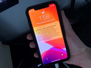 A person holds a cellphone with an emergency alert on the screen.