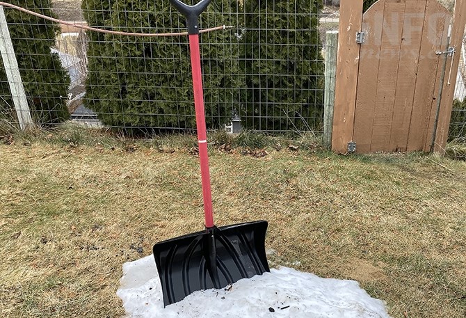 A shovel in a small patch of snow surrounded by a brown lawn.