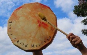 Someone hitting a drum that says every child matters.