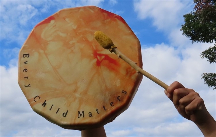 Someone hitting a drum that says every child matters.