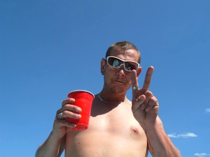 Shirtless man holds up a "peace" sign.