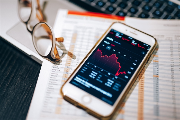 A phone with a stock graph going down, some charts and glasses.