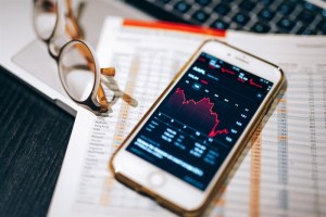 A phone with a stock graph going down, some charts and glasses.