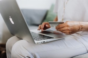 A woman holds a credit card and has a laptop on her lap.