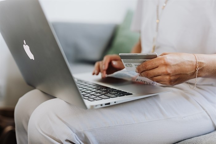 A woman holds a credit card and has a laptop on her lap.