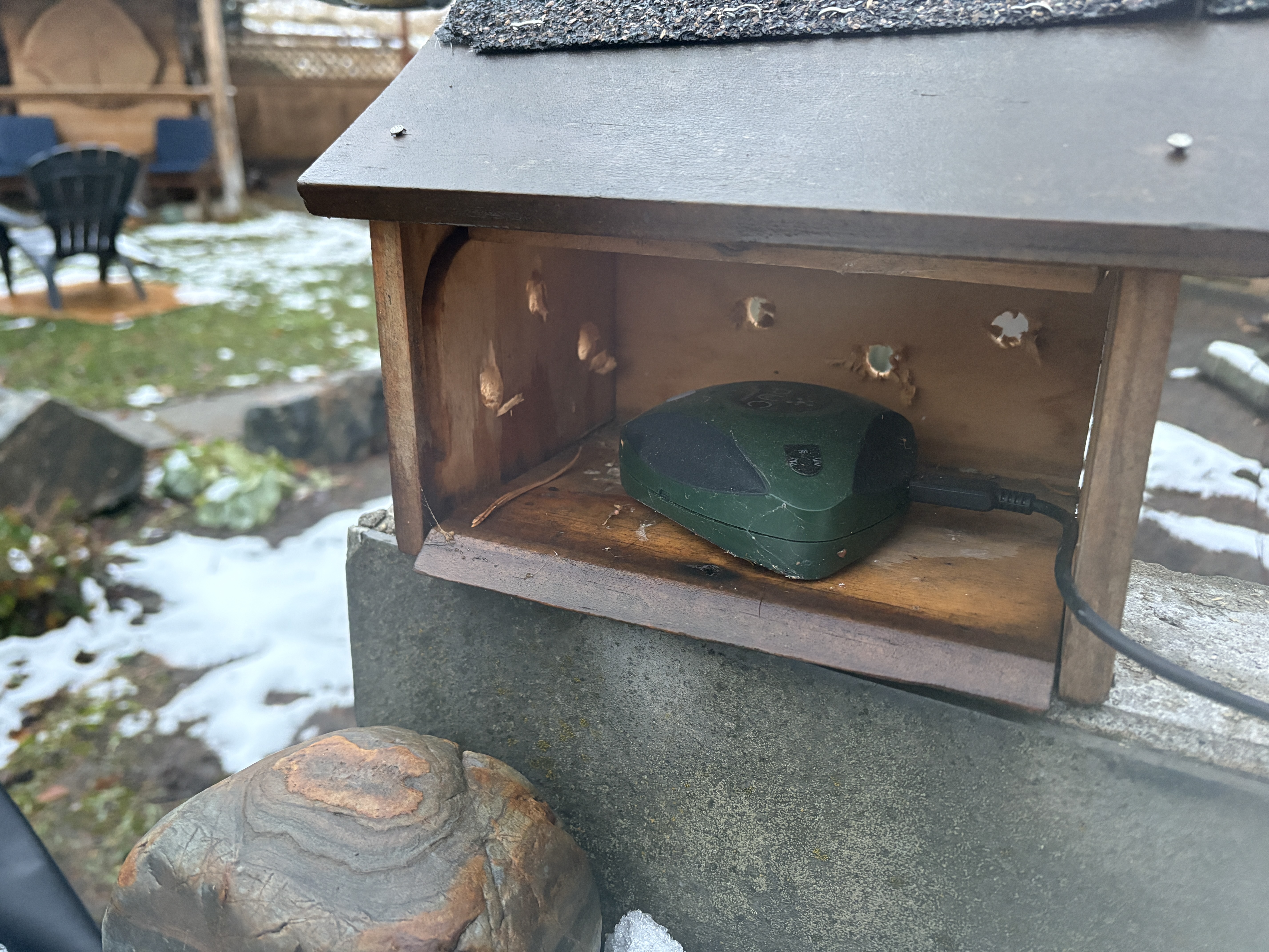 A green plastic device the size of a hardball sits in a wooden birdhouse.
