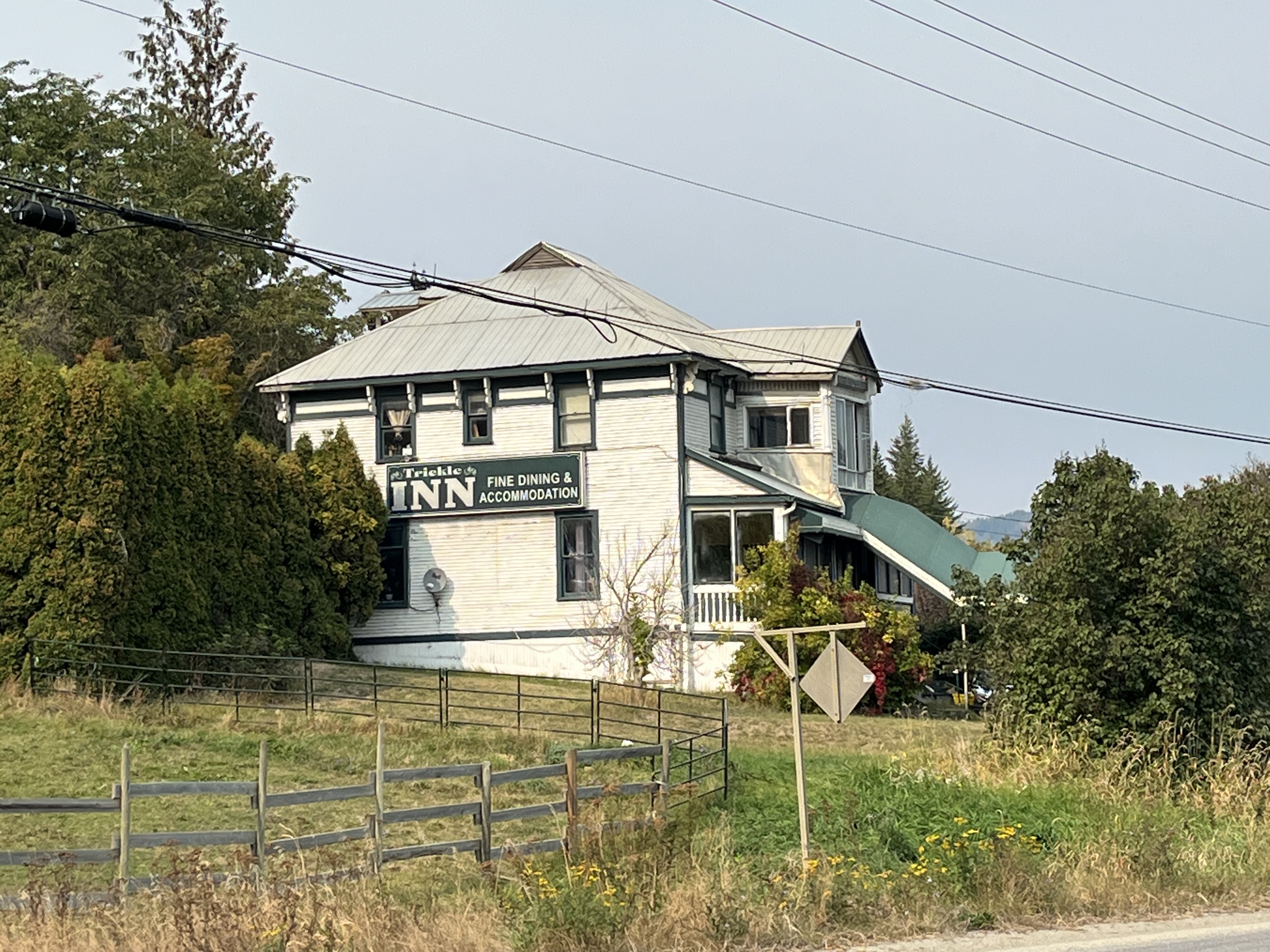 A big old white house with green trim sits on a green grassy property.