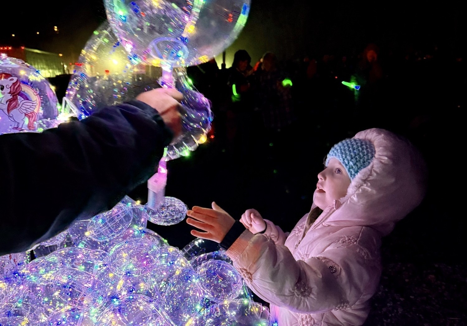 A child in a winter coat reaches up to receive a balloon.