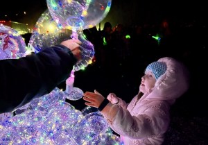 A child in a winter coat reaches up to receive a balloon.