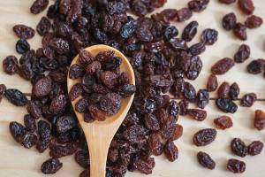 A wooden spoon holding raisins is positioned over a pile of raisins.
