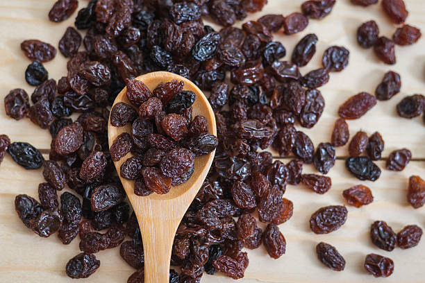 A wooden spoon holding raisins is positioned over a pile of raisins.