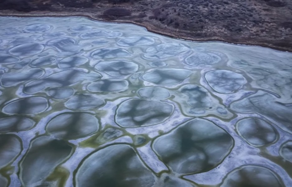 A frozen lake has colourful spots on its surface.