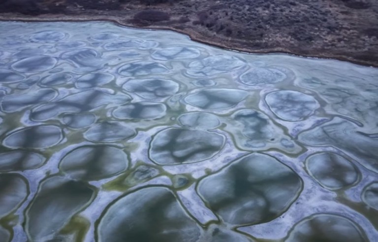 A frozen lake has colourful spots on its surface.