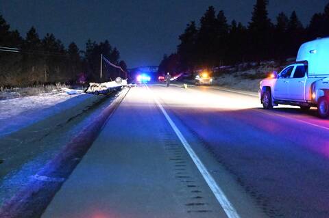 A dark image of police lights and an overturned pickup truck on the road.