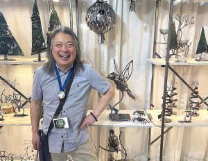 A man stands with his hand on his hip wearing a smile in front of metal sculptures.