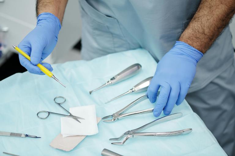 A doctor wearing gloves selects a medical surgery instrument.