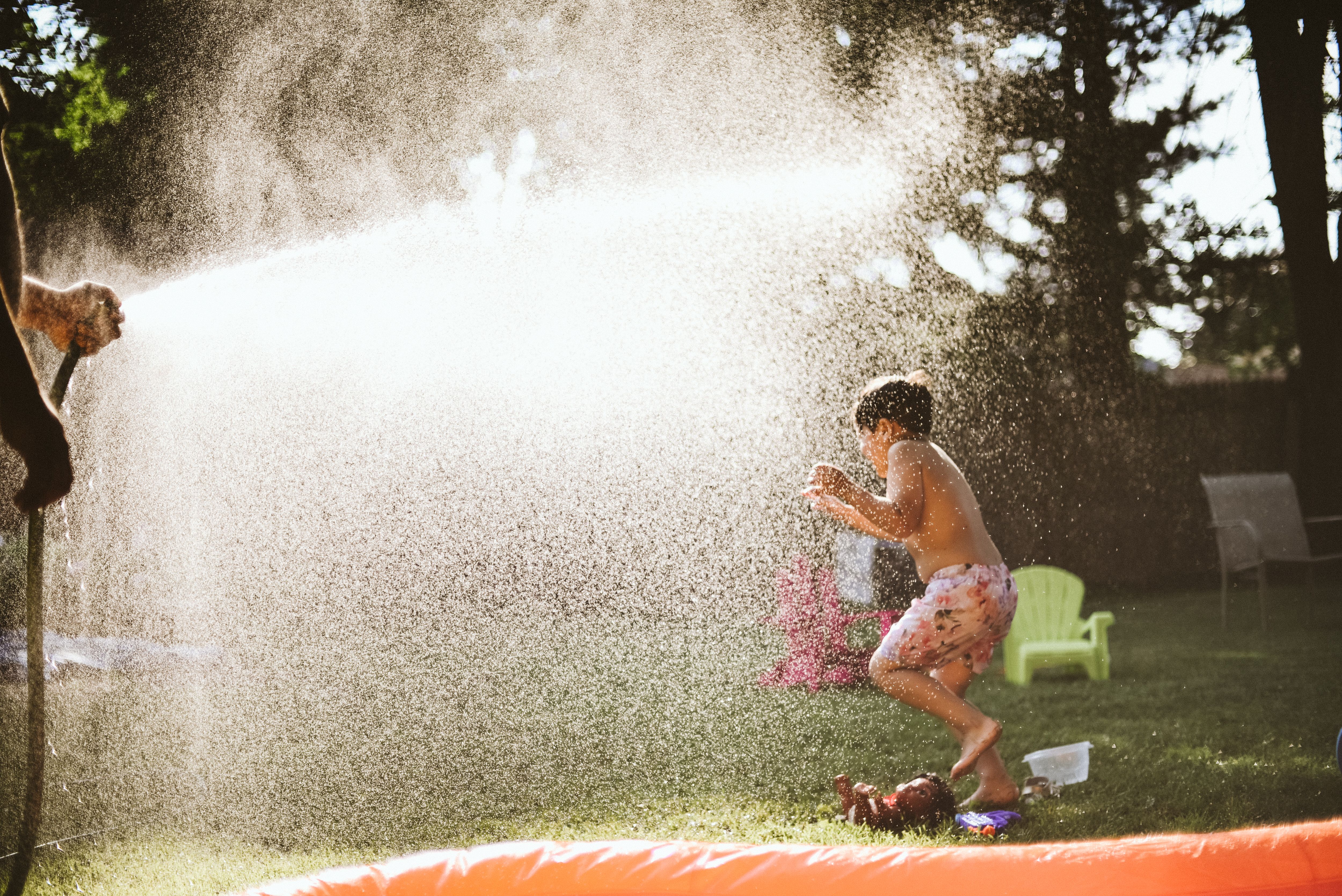 A child playing in water sprayed from a garden hose.