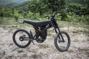 An e-bike parked on a vacant lot with bushes in the background.