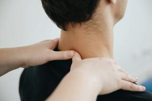 A physiotherapist puts both hands on a client's neck.