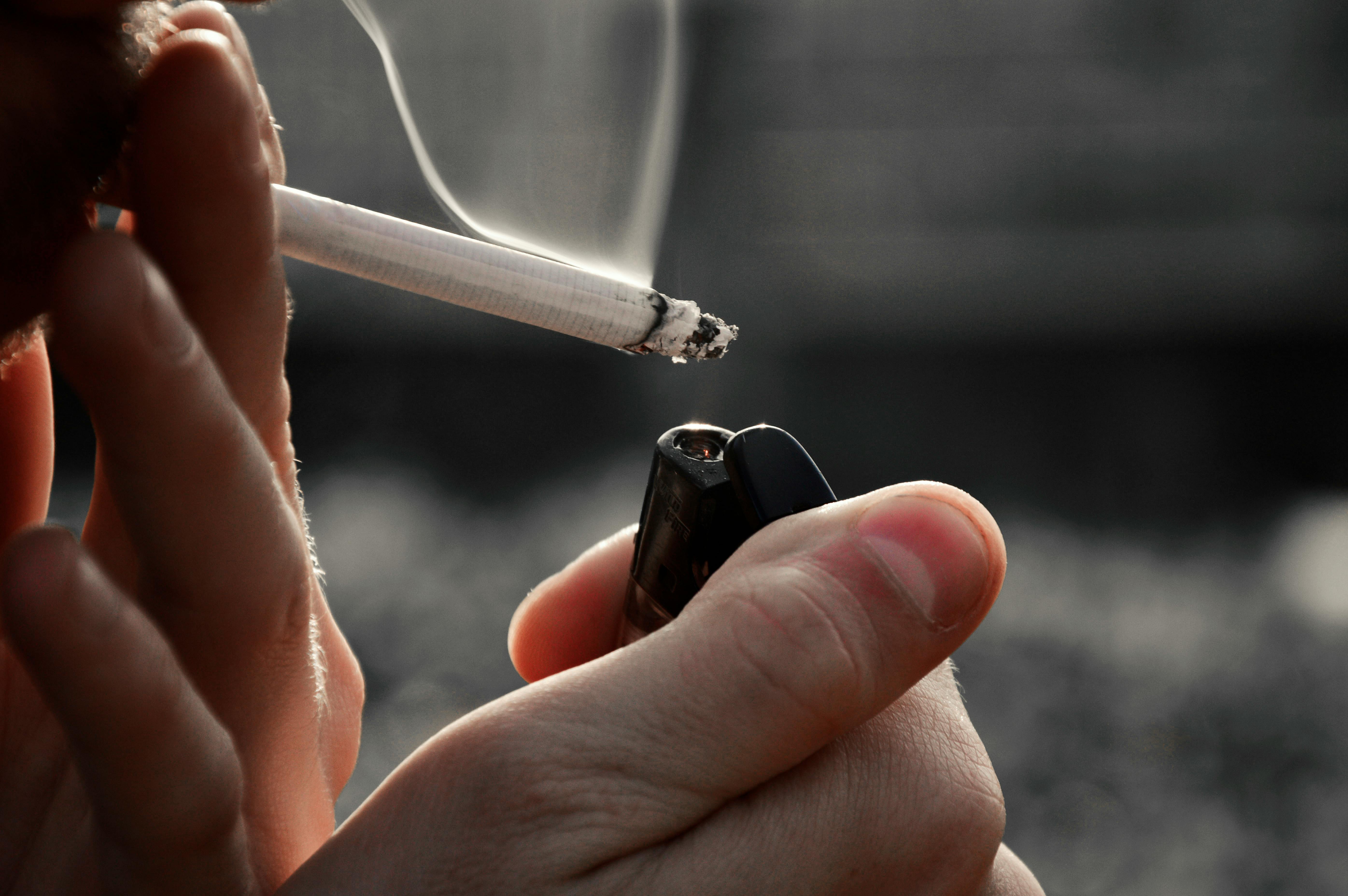 A hand holds a cigarette lighter and lights a cigarette.