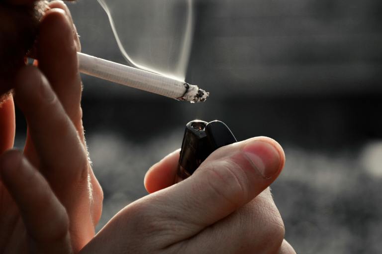 A hand holds a cigarette lighter and lights a cigarette.