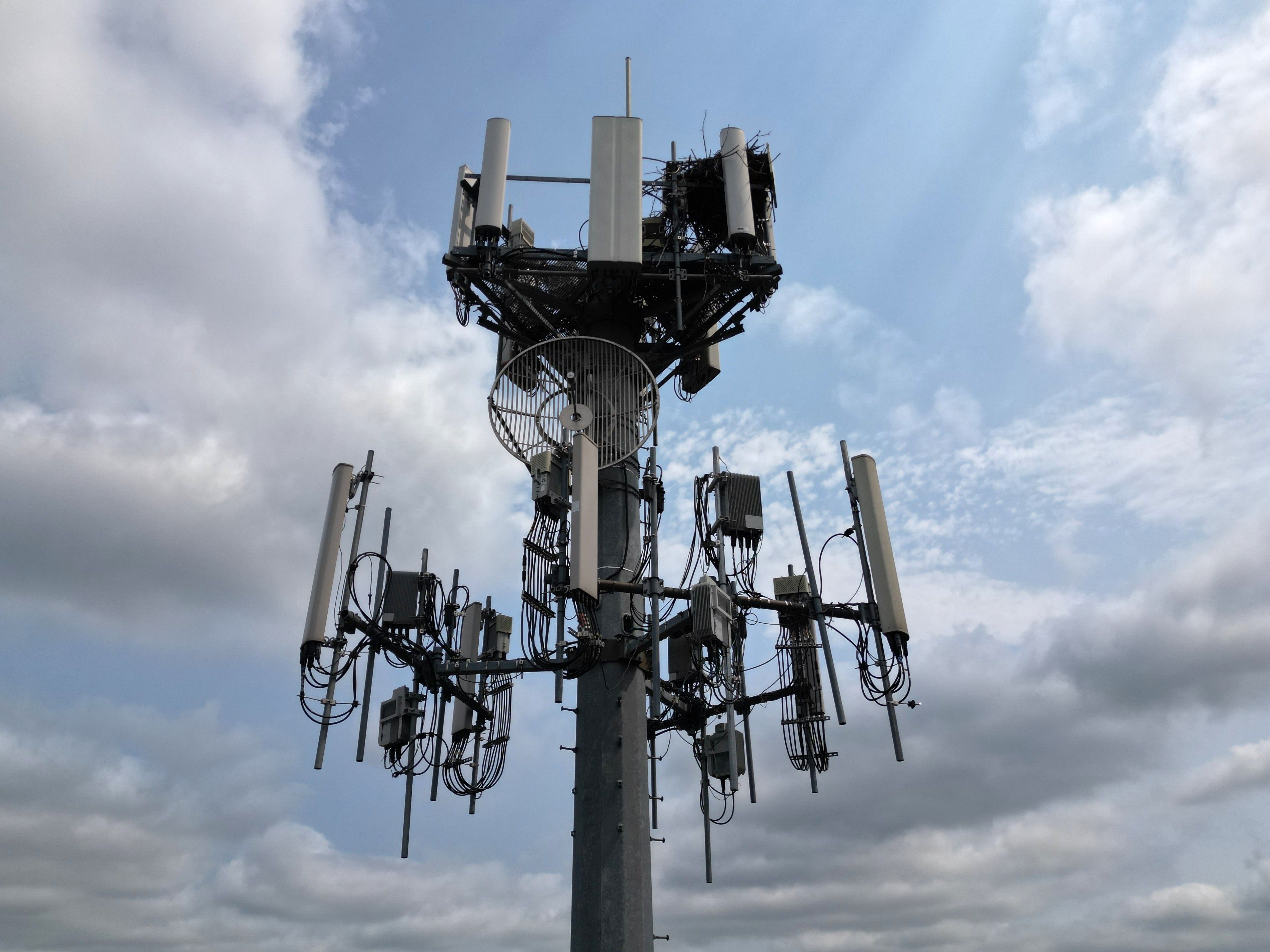 A cellphone tower with a mix of blue sky and clouds in the background.