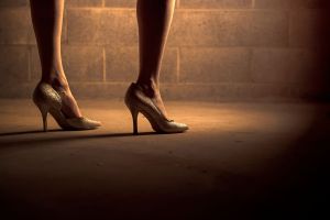 a woman in high heels stands next to a wall.