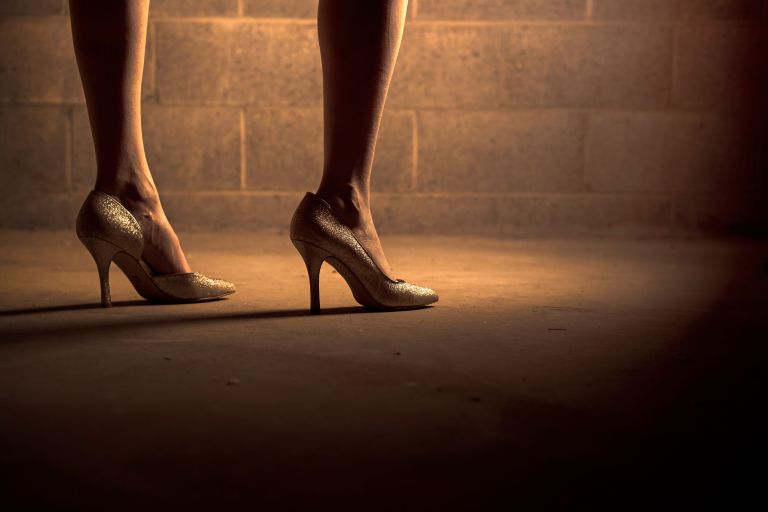 a woman in high heels stands next to a wall.