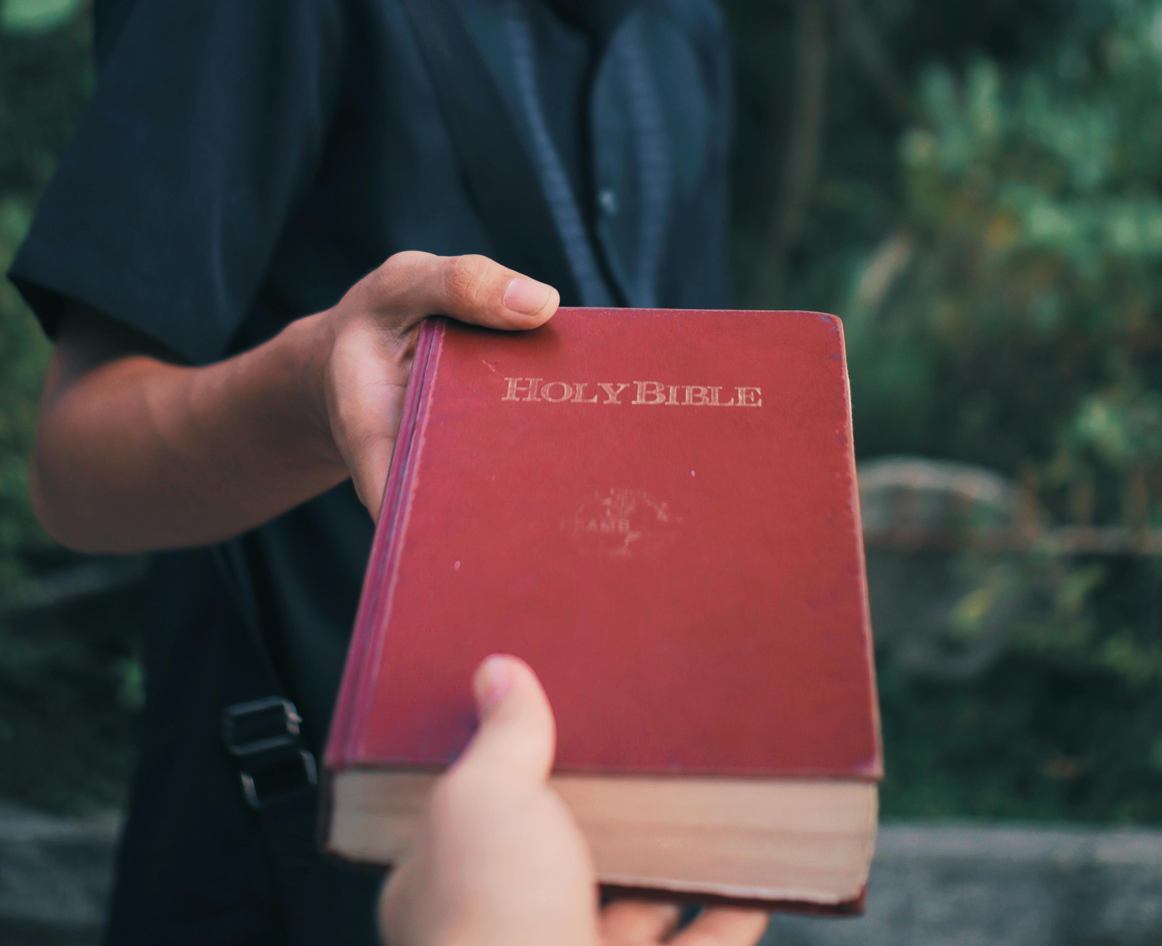 A person puts a copy of the bible into someone's hand.