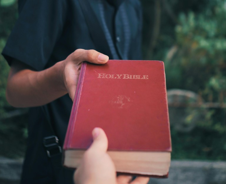A person puts a copy of the bible into someone's hand.