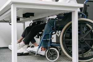 Two people in wheelchairs sit under a desk