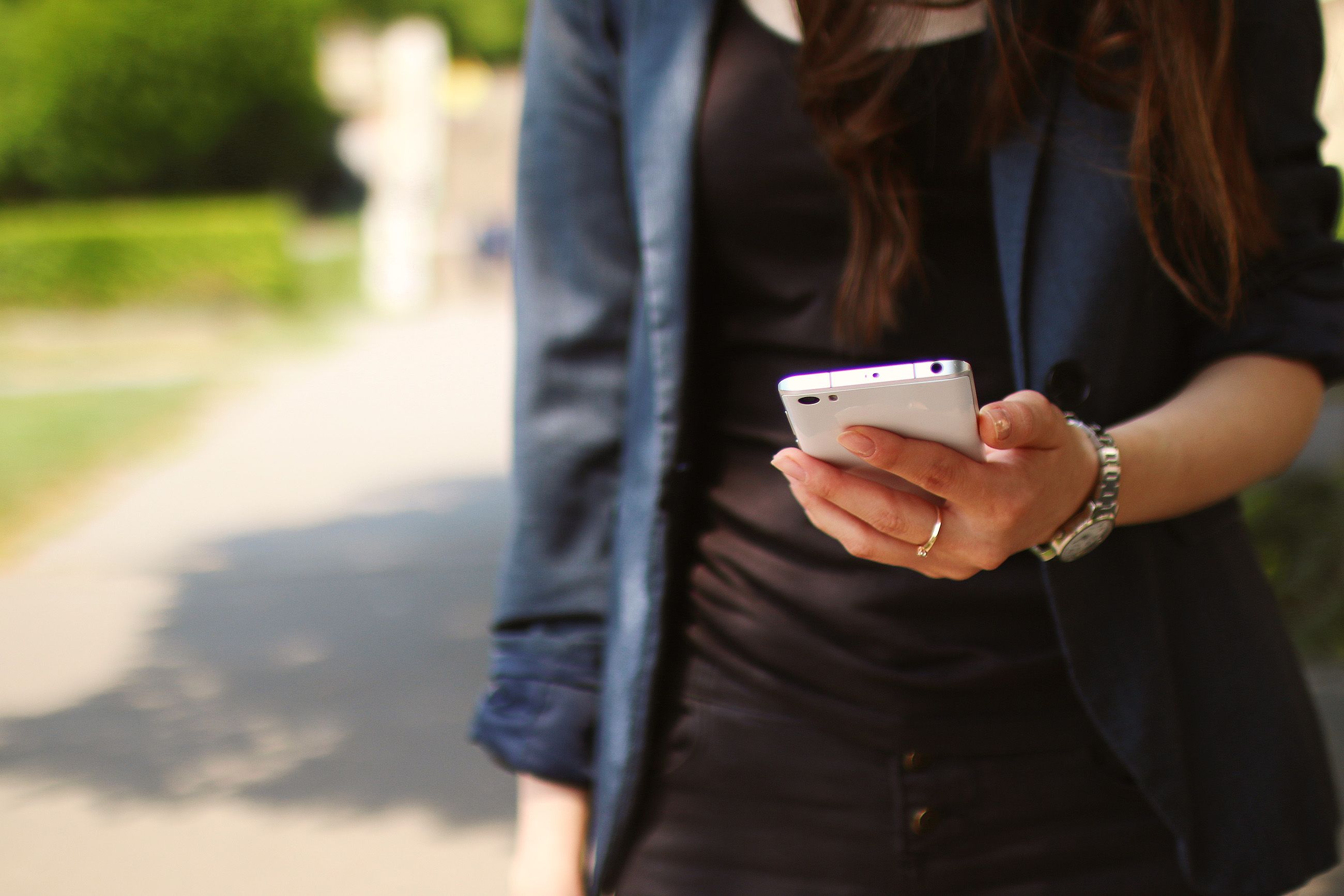 A woman walking with a smartphone in her hand on a sunny day.