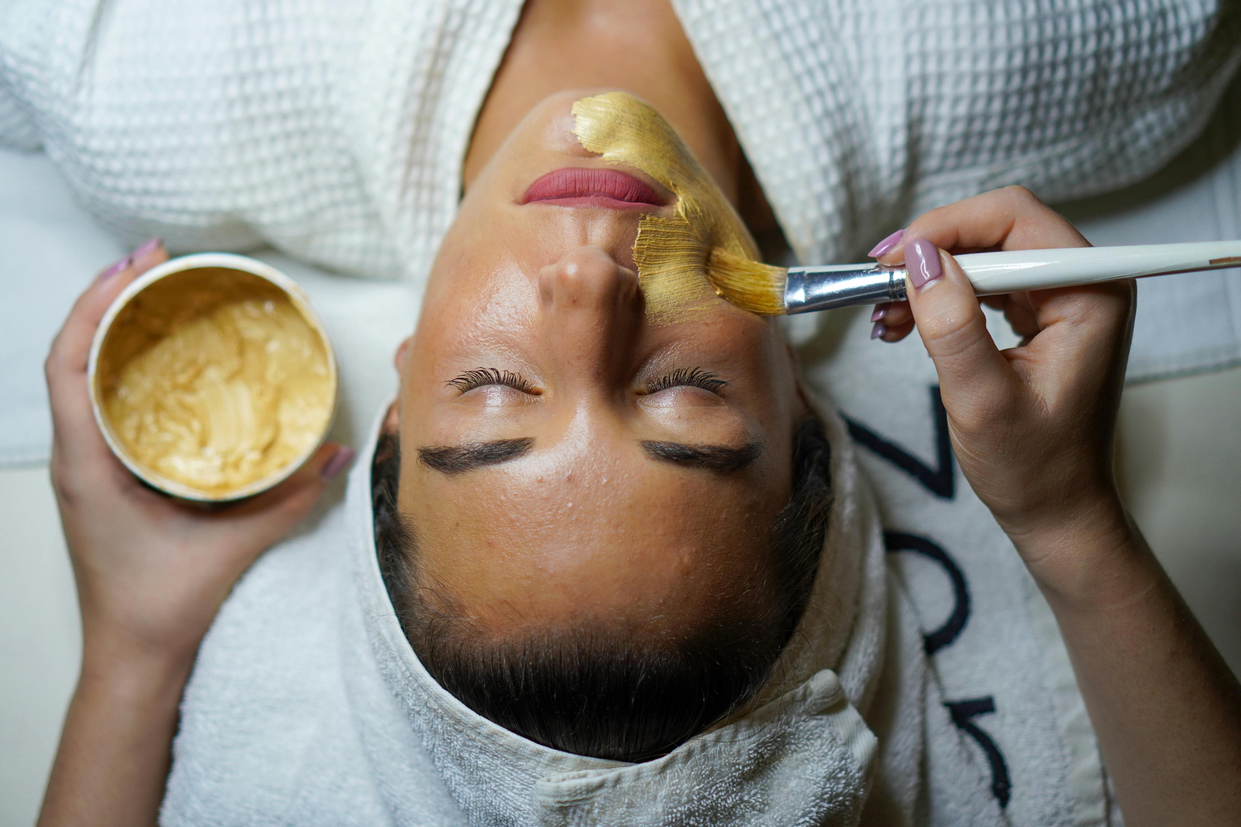 A person applies a beauty product to a woman's face during a spa treatment.