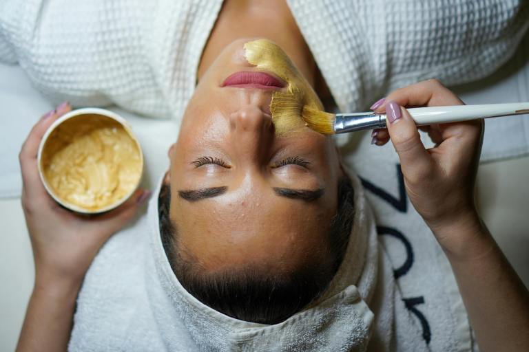 A person applies a beauty product to a woman's face during a spa treatment.