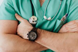 A doctor in a green shirt folds his arms and has a stethoscope around his neck.